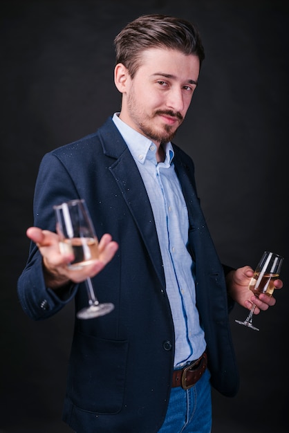 Junger Mann in der blauen Stellung mit Champagnergläsern in den Händen