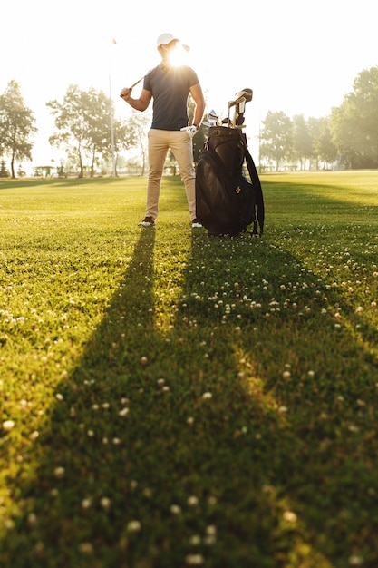 Junger Mann in der Kappe, die Golfschläger hält