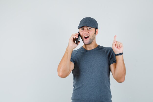 Junger Mann in der T-Shirt-Kappe, die ausgezeichnete Idee findet, während er auf Handy spricht