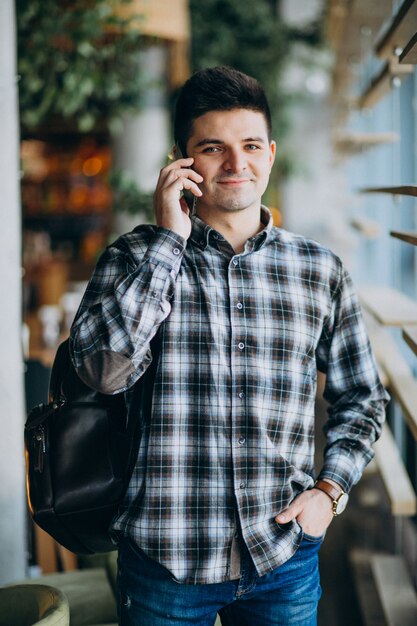 Junger Mann in einem Café, das das Fenster bereitsteht und am Telefon spricht