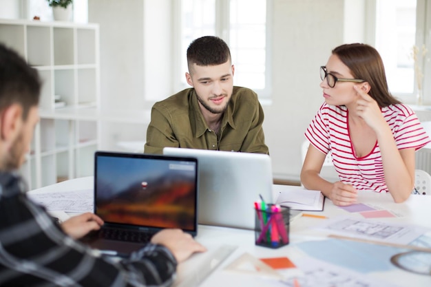 Junger Mann in Hemd und Frau in gestreiftem T-Shirt und Brille, die mit Laptop zusammenarbeiten Gruppe cooler Jungs, die Zeit im modernen Büro verbringen