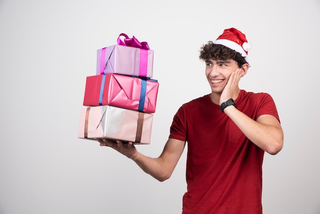 Junger Mann in Santa Hut, der glücklich Geschenke betrachtet.