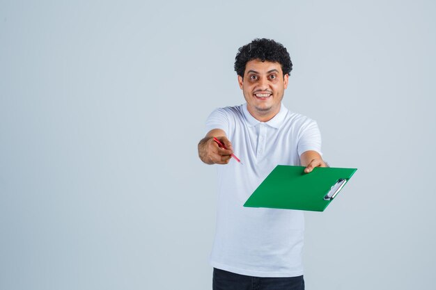 Junger Mann in weißem T-Shirt und Jeans, der der Kamera Notizbuch und Stift präsentiert und glücklich aussieht, Vorderansicht.