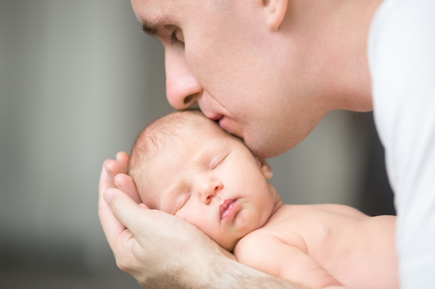 Junger Mann küsst ein Neugeborenes, er hält in seinen Handflächen