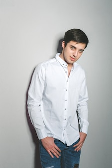 Junger mann kurz gesagt und weißes hemd lächelt, stehend nahe der wand mit gläsern