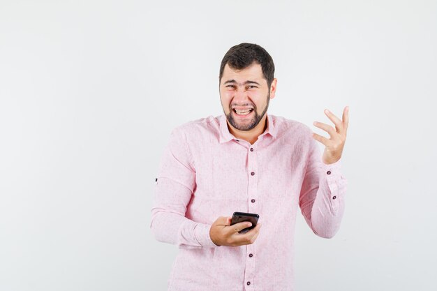 Junger Mann lacht, während Handy in rosa Hemd hält und glücklich schaut