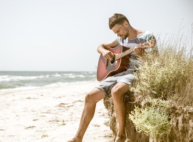 Junger Mann mit Akustikgitarre am Strand