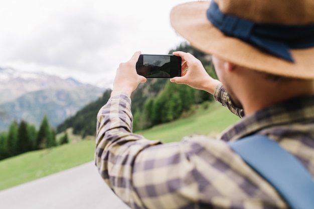 Junger Mann mit blauem Rucksack macht ein Bild von der Landschaft, die zu den Bergen geht