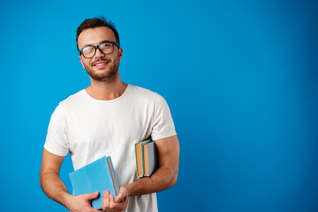 Junger Mann mit Brille steht und liest ein Buch vor blauem Hintergrund