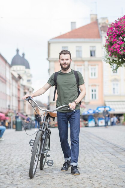 Junger Mann mit dem Fahrrad gehend auf Straße