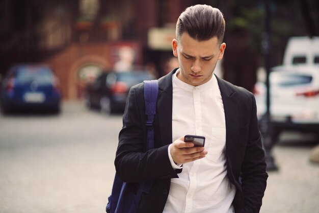 Junger Mann mit dem Rucksack, der ein Telefon hält