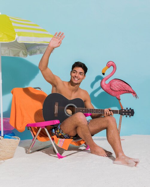 Junger Mann mit der wellenartig bewegenden Hand der Gitarre auf Strand