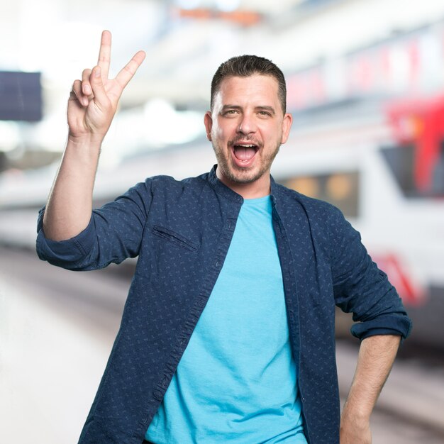 Junger Mann mit einem blauen Outfit tragen. Doing Sieg Geste.