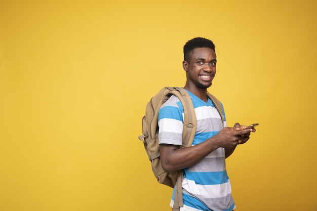 Junger Mann mit einem Rucksack mit seinem Telefon vor einem gelben Hintergrund