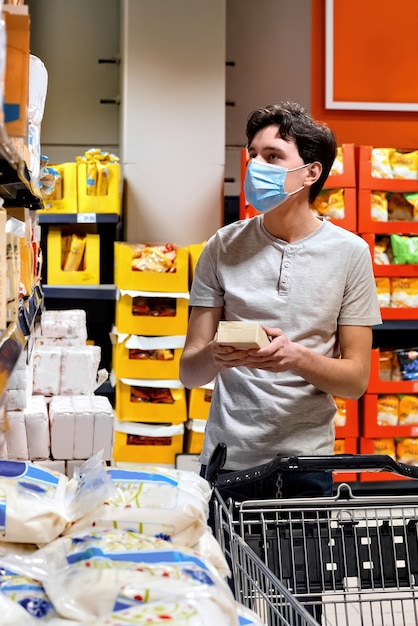 Junger Mann mit einer Gesichtsmaske, die Snacks in einem Supermarkt betrachtet