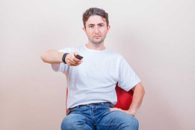 Junger Mann mit Fernbedienung beim Sitzen auf Stuhl in T-Shirt und Jeans