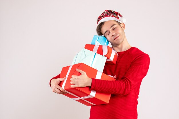 Junger Mann mit geschlossenem Auge der Vorderansicht mit Weihnachtsmütze, der seine Geschenke auf weißem Hintergrundkopierraum festhält