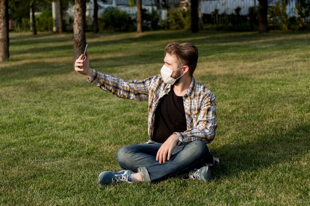 Junger Mann mit Gesichtsmaske, die ein selfie draußen nimmt