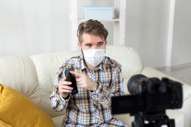 Junger mann mit gesichtsmaskenaufzeichnungsvideo zu hause