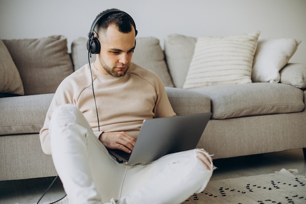 Junger Mann mit Kopfhörern und Computer zu Hause