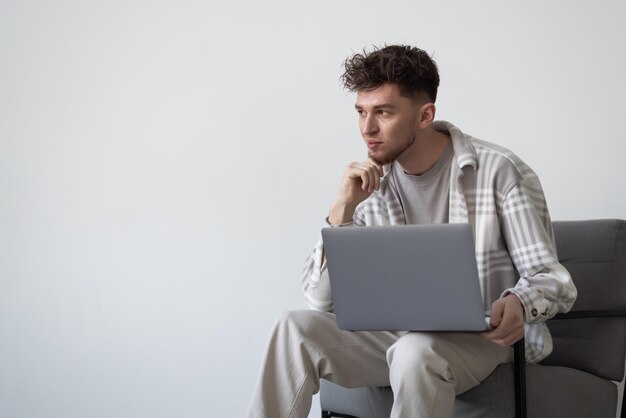 Junger Mann mit Laptop auf Stuhl isoliert auf weißem Hintergrund entspannen