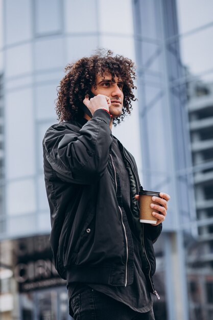 Junger Mann mit lockigem Haar, der Kaffee trinkt und telefoniert
