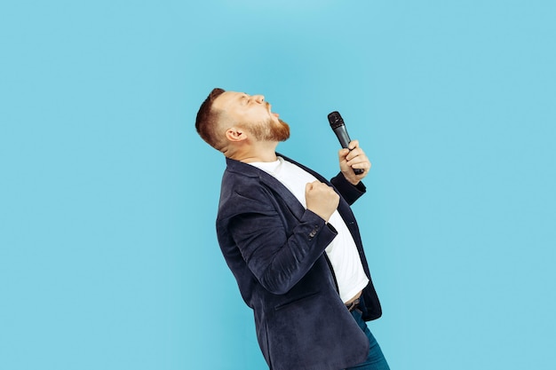 Kostenloses Foto junger mann mit mikrofon auf blauer wand