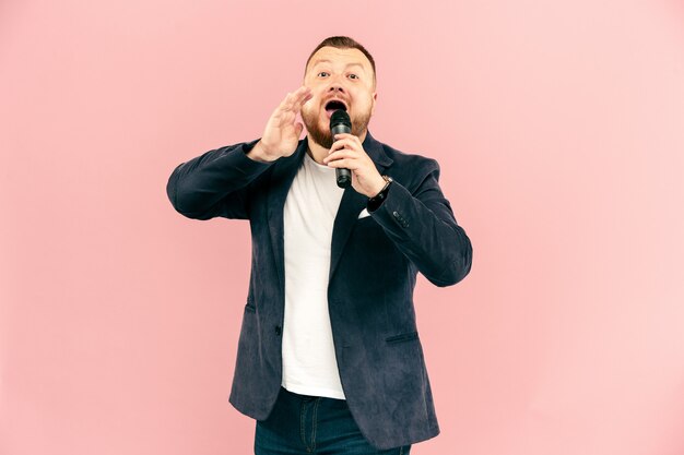 Junger Mann mit Mikrofon auf rosa Wand, führend mit Mikrofon