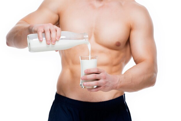 Junger Mann mit perfektem Körper, der Milch in ein Glas gießt - lokalisiert auf weißer Wand.