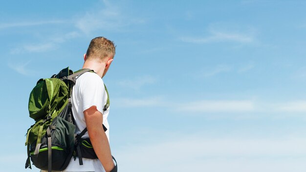 Junger Mann mit reisendem Rucksack gegen Hintergrund des blauen Himmels