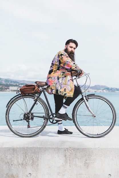 Kostenloses Foto junger mann mit seinem fahrrad auf wellenbrecher nahe der küste