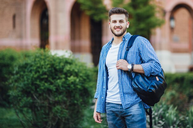 Junger Mann mit Sonnenbrille und in einem weißen Hemd mit grauer Hose, der mit einer Tasse Kaffee auf seinem Telefon spricht