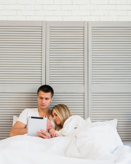 Junger Mann mit Tablette nahe schlafender Frau im Bett