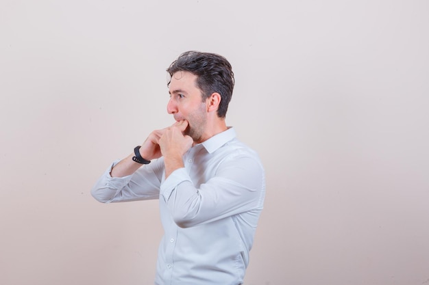 Junger mann pfeift mit den fingern im weißen hemd und sieht optimistisch aus looking