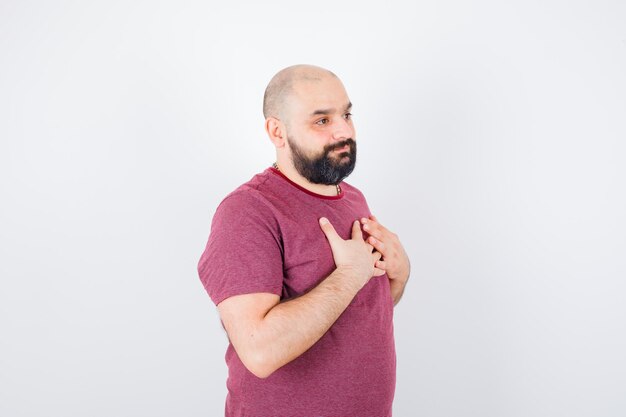 Kostenloses Foto junger mann ruht die hände auf der brust in rosa t-shirt und sieht optimistisch aus, vorderansicht.