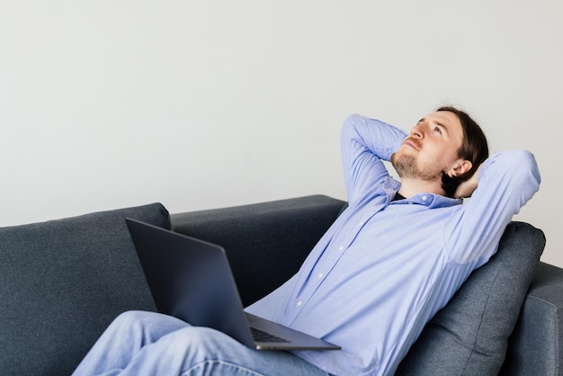 Junger Mann ruht sich mit einem Laptop auf einer Couch aus