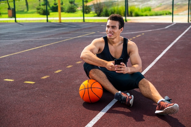 Junger Mann sitzt auf dem Basketballplatz
