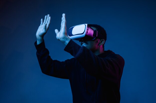 Junger Mann spielt in VR-Brille im Neonlicht auf Blau