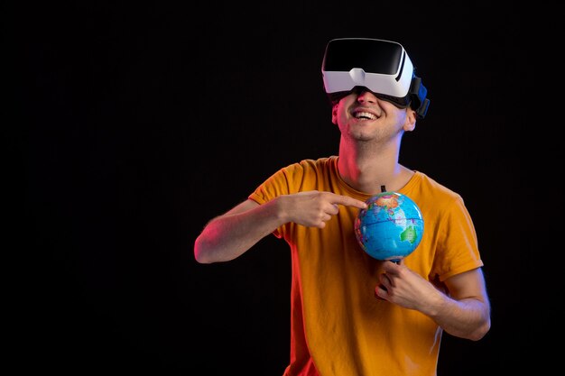 Junger Mann spielt virtuelle Realität, die Globus auf dunkler Oberfläche hält