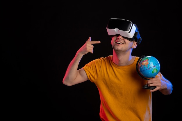Junger Mann spielt virtuelle Realität, die Globus auf dunkler Oberfläche hält