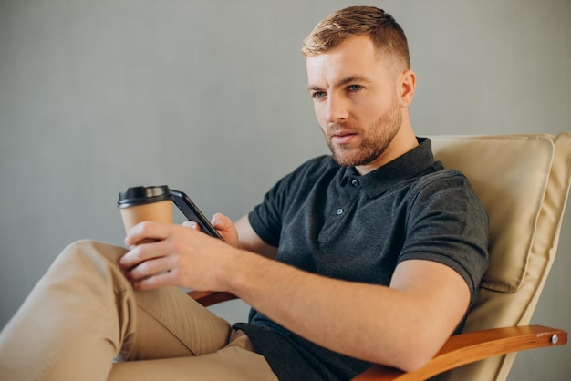 Junger Mann trinkt Kaffee in einem bequemen Stuhl