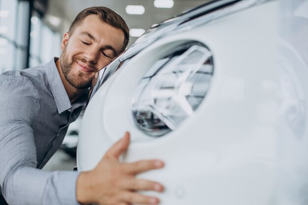 Junger Mann umarmt sein neues Auto in einem Autosalon