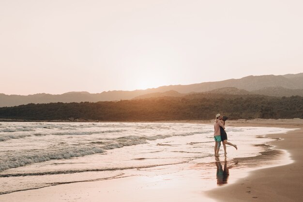 Junger Mann und Frau, die am Strand bei Sonnenuntergang küssen.