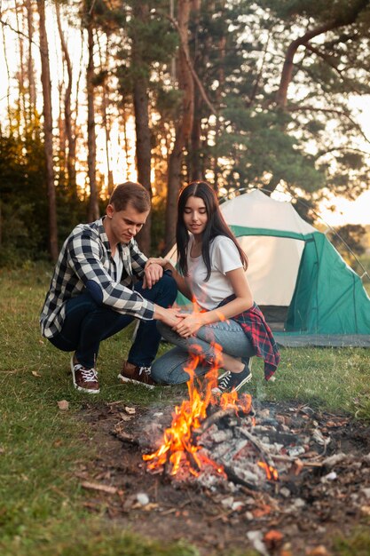 Junger Mann und Frau, die ein Lagerfeuer im Freien haben