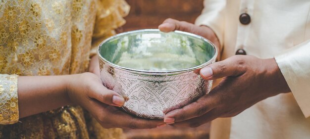 Junger Mann und Frau in wunderschönen thailändischen Kostümen, die eine Wasserschüssel im Tempel halten und die gute Kultur der Thailänder während des Songkran-Festivals am thailändischen Neujahrs-Familientag im April bewahren