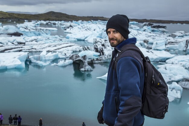 Junger Mann vor kleinen blauen Eisbergen im Jokulsarlon-Eissee und sehr grauem Himmel in Island