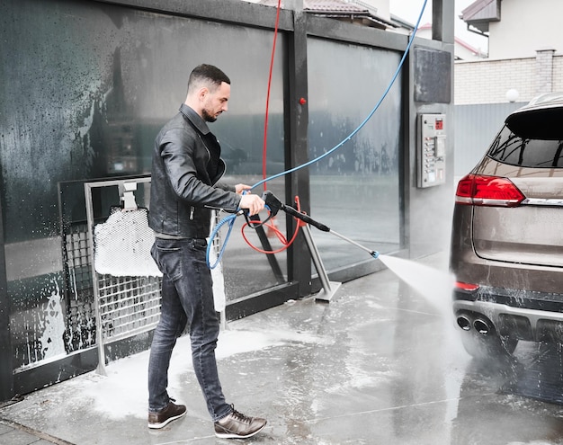 Junger Mann wäscht Auto auf Autowaschanlage im Freien