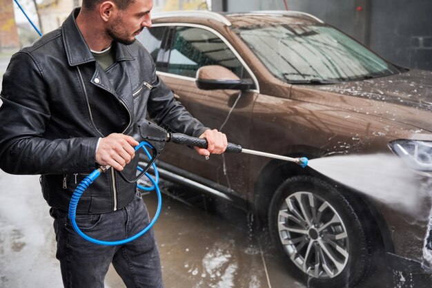 Junger Mann wäscht Auto auf Autowaschanlage im Freien