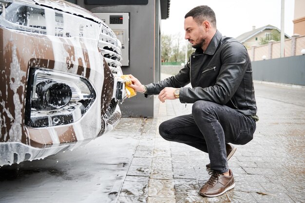 Junger Mann wäscht Auto auf Autowaschanlage im Freien