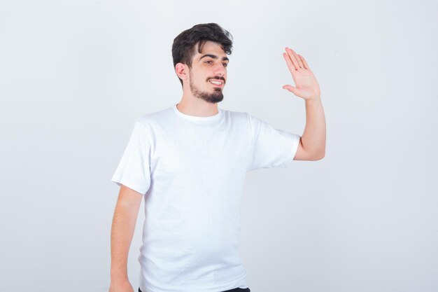 Junger Mann winkt mit der Hand, um sich im T-Shirt zu verabschieden und sieht fröhlich aus